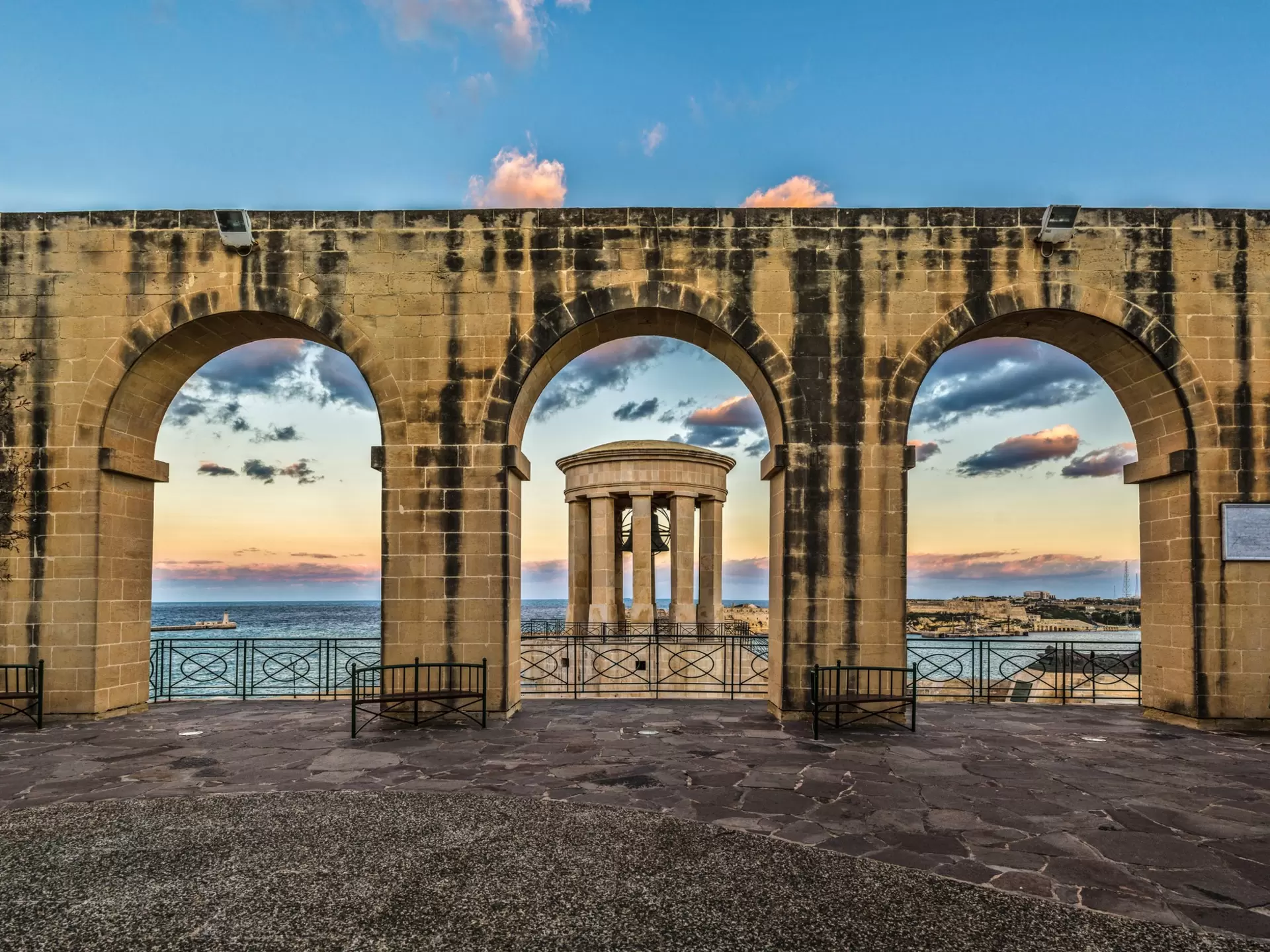 A large brick wall with archways framing a rotunda with a bell that stands out at sea.