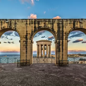 A large brick wall with archways framing a rotunda with a bell that stands out at sea.