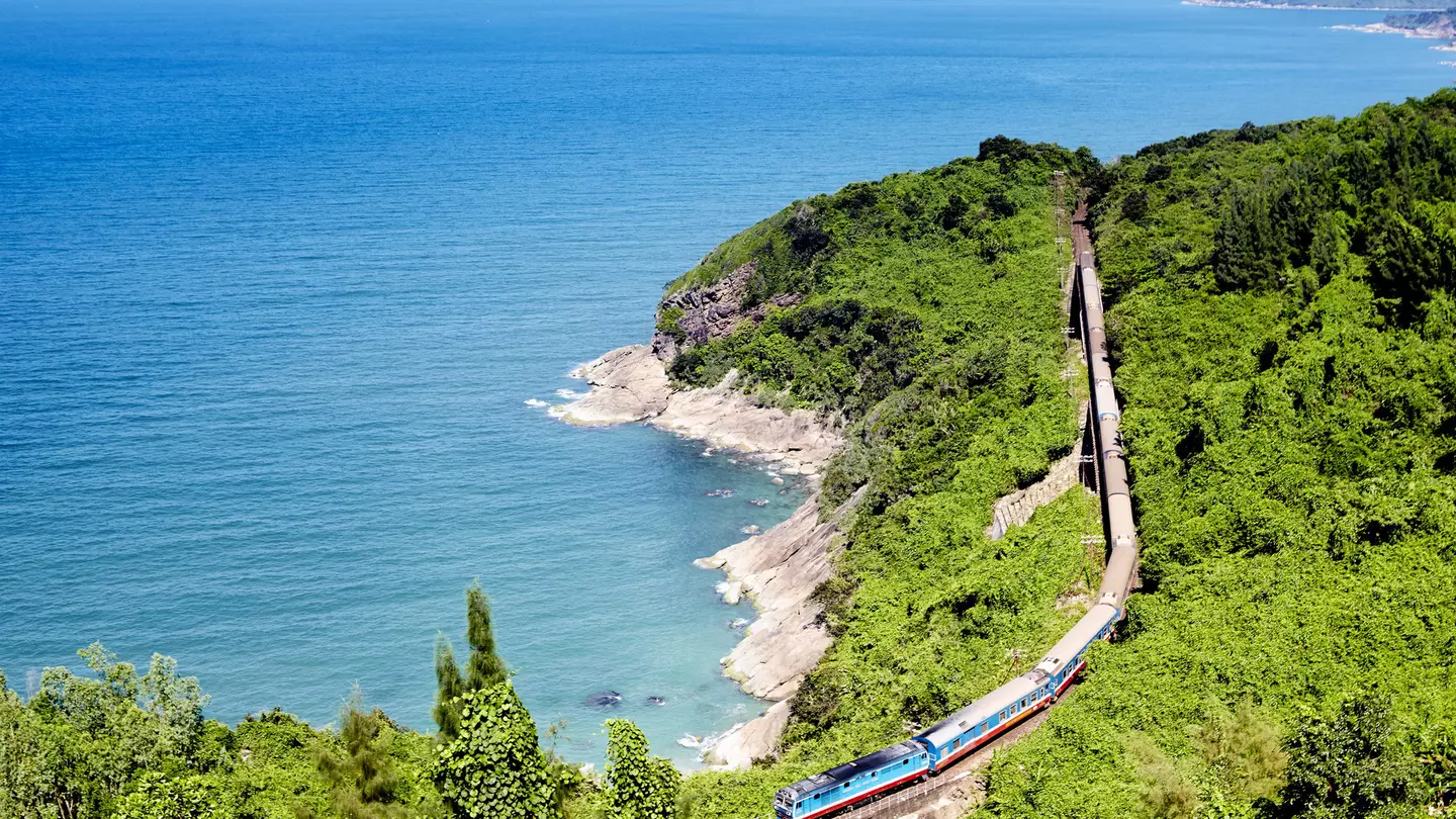 A train on a track running through a green landscape along the coast of Vietnam.
