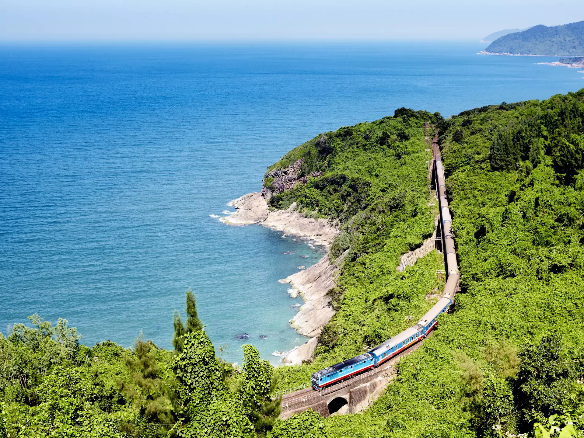 A train on a track running through a green landscape along the coast of Vietnam.