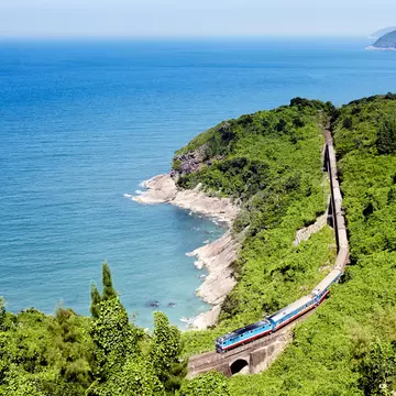 A train on a track running through a green landscape along the coast of Vietnam.