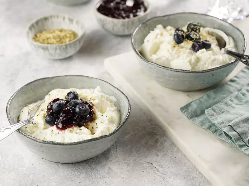 Two bowls filled with a plain white yoghurt-like breakfast topped with jam, fresh blueberries and hemp seeds.