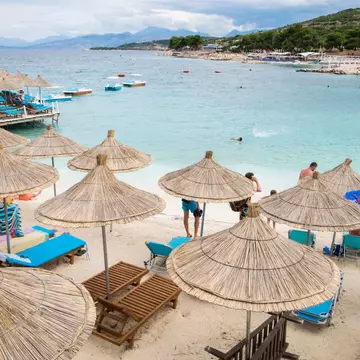 Sun umbrellas on the beach at Ksamil, Albania, with a blue bay behind.