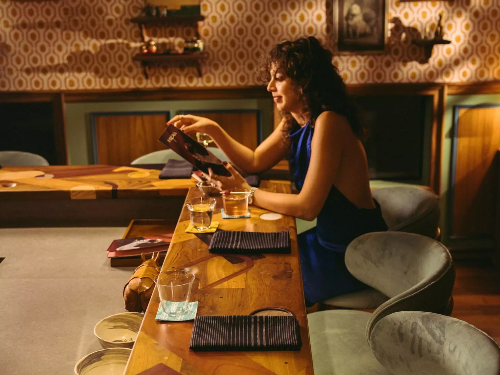 A lone woman sits a chef counter in a dimly lit restaurant holding a menu.