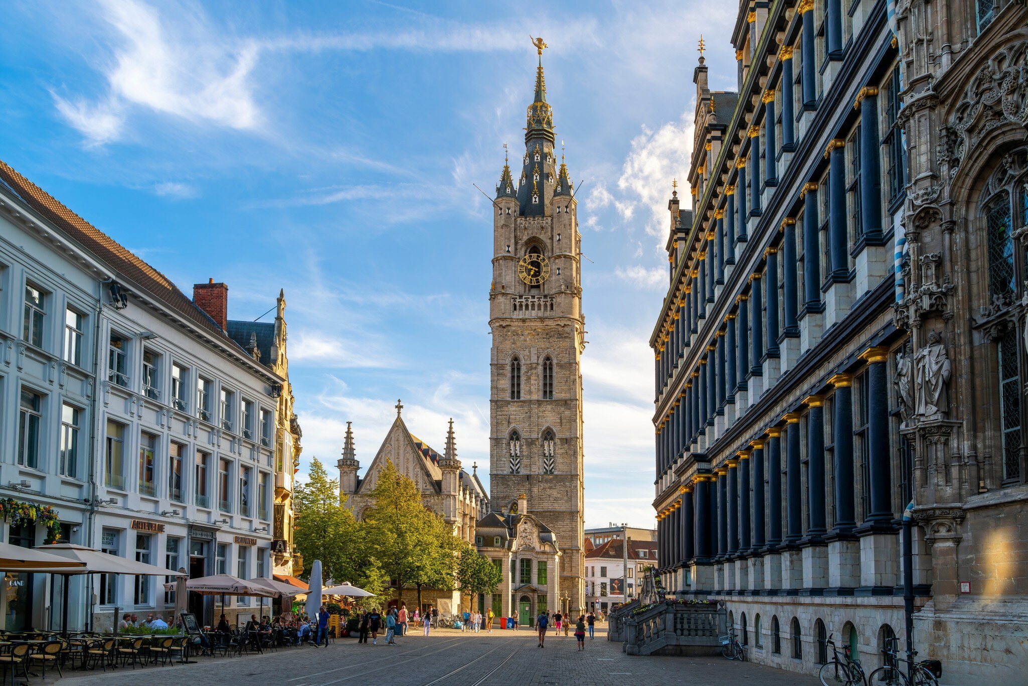 Ghent, Belgium - August 18 2023: Sunlight shines on the medieval Ghent Belfry tower, or Het Belfort van Gent, with City Hall on the right and sidewalk cafes on the left, in the historic old town., License Type: media, Download Time: 2025-12-03T11:22:23.000Z, User: aniabartoszek, Editorial: true, purchase_order: 56530 - Guidebooks, job: Global Publishing-WIP, client: Belgium & Luxembourg 10, other: Ania Lenihan