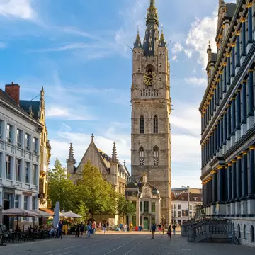 Ghent, Belgium - August 18 2023: Sunlight shines on the medieval Ghent Belfry tower, or Het Belfort van Gent, with City Hall on the right and sidewalk cafes on the left, in the historic old town., License Type: media, Download Time: 2025-12-03T11:22:23.000Z, User: aniabartoszek, Editorial: true, purchase_order: 56530 - Guidebooks, job: Global Publishing-WIP, client: Belgium & Luxembourg 10, other: Ania Lenihan