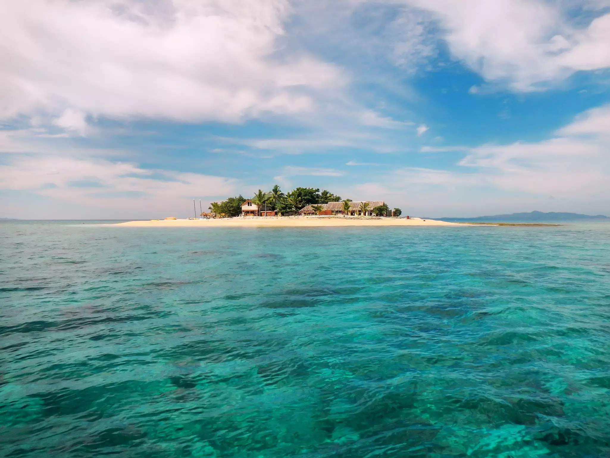 Small huts sit on a picturesque island in the middle of the ocean.