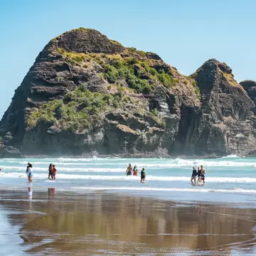 People paddling in the water at Piha beach with the Camel Rock in the background. 