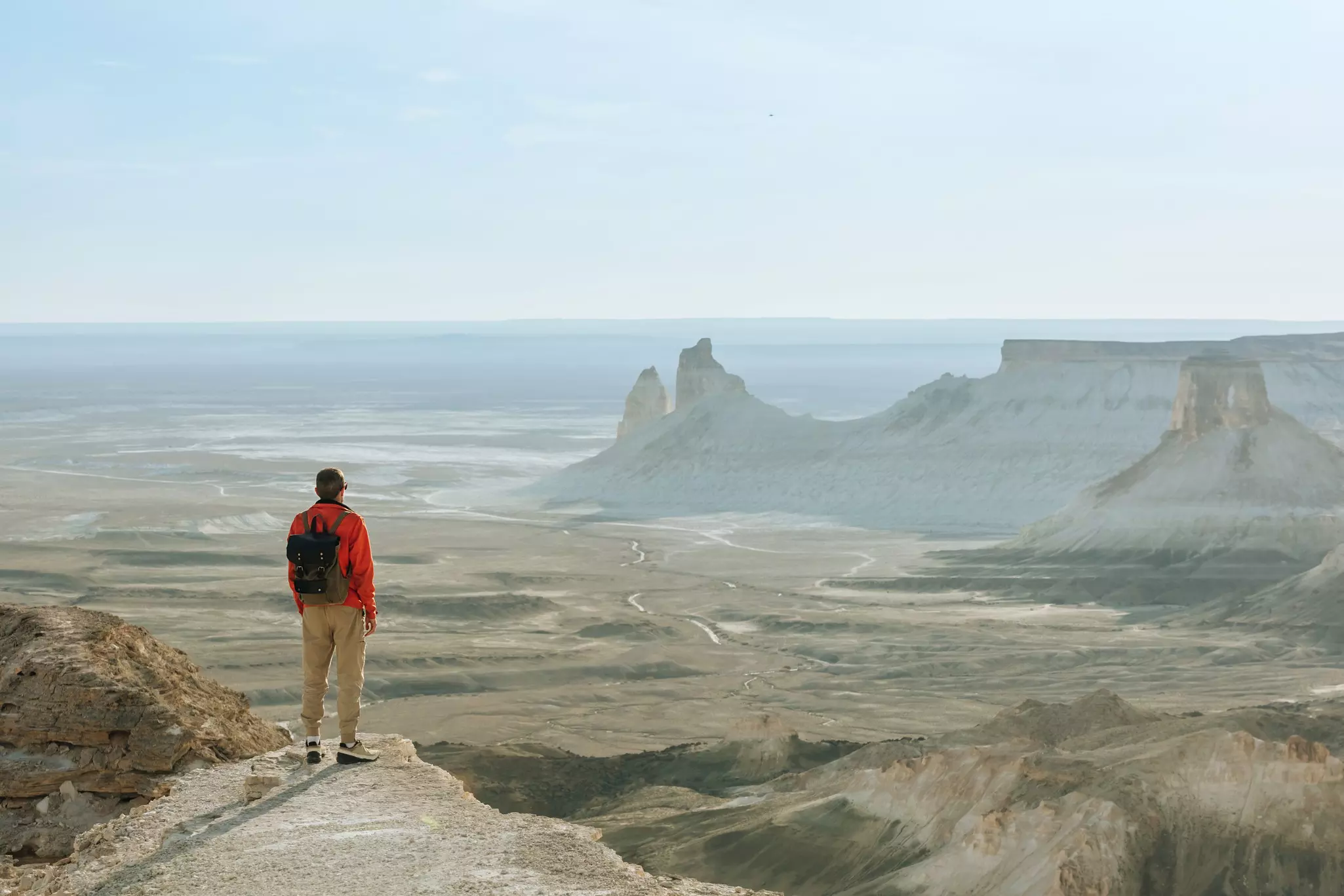 A hiker at the top of a mountain looking out at mountains that rise from a flat landscape.