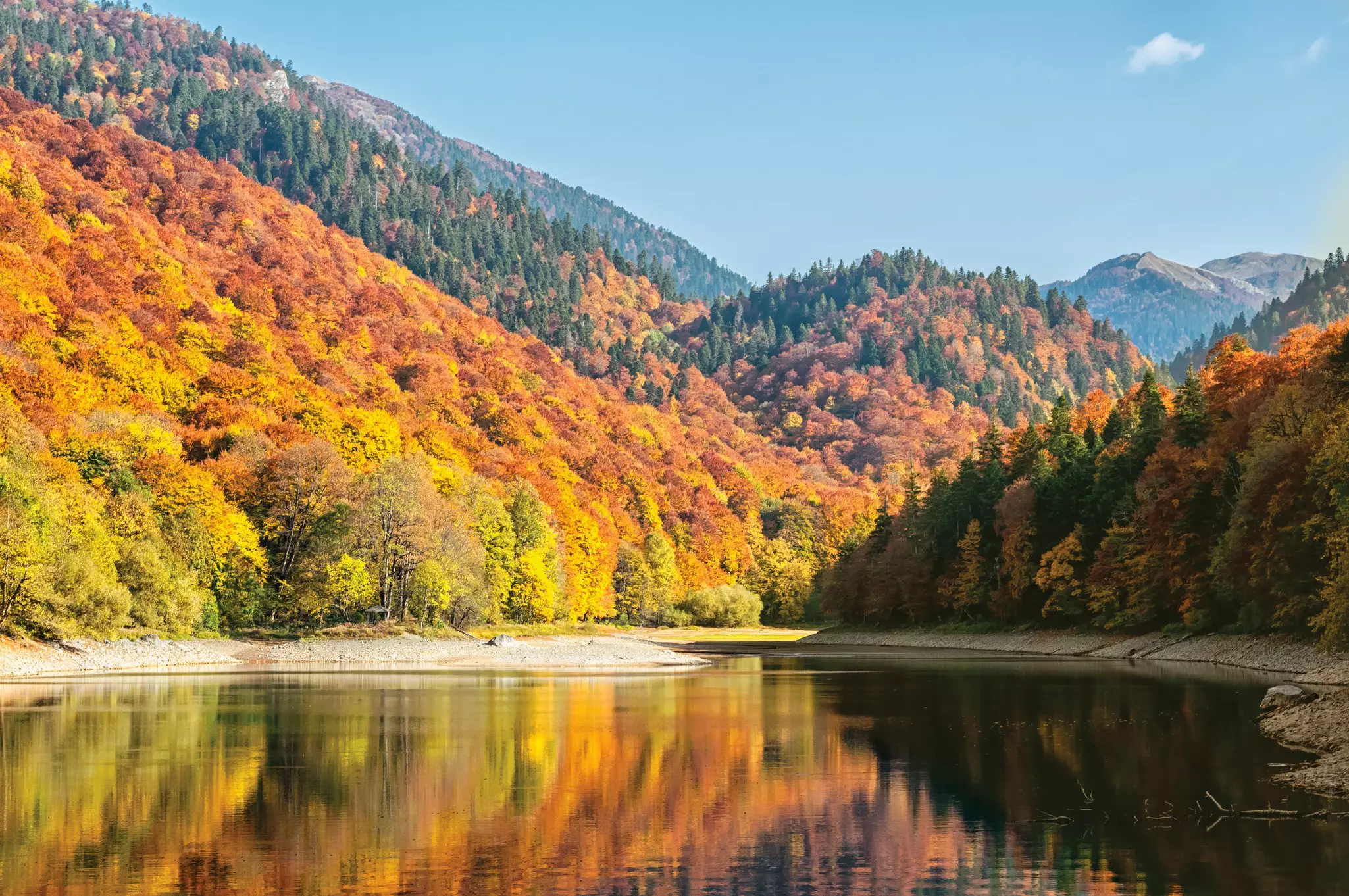 A lake in Montenegro surrounded by trees with yellow, orange and red leaves reflects the colors.