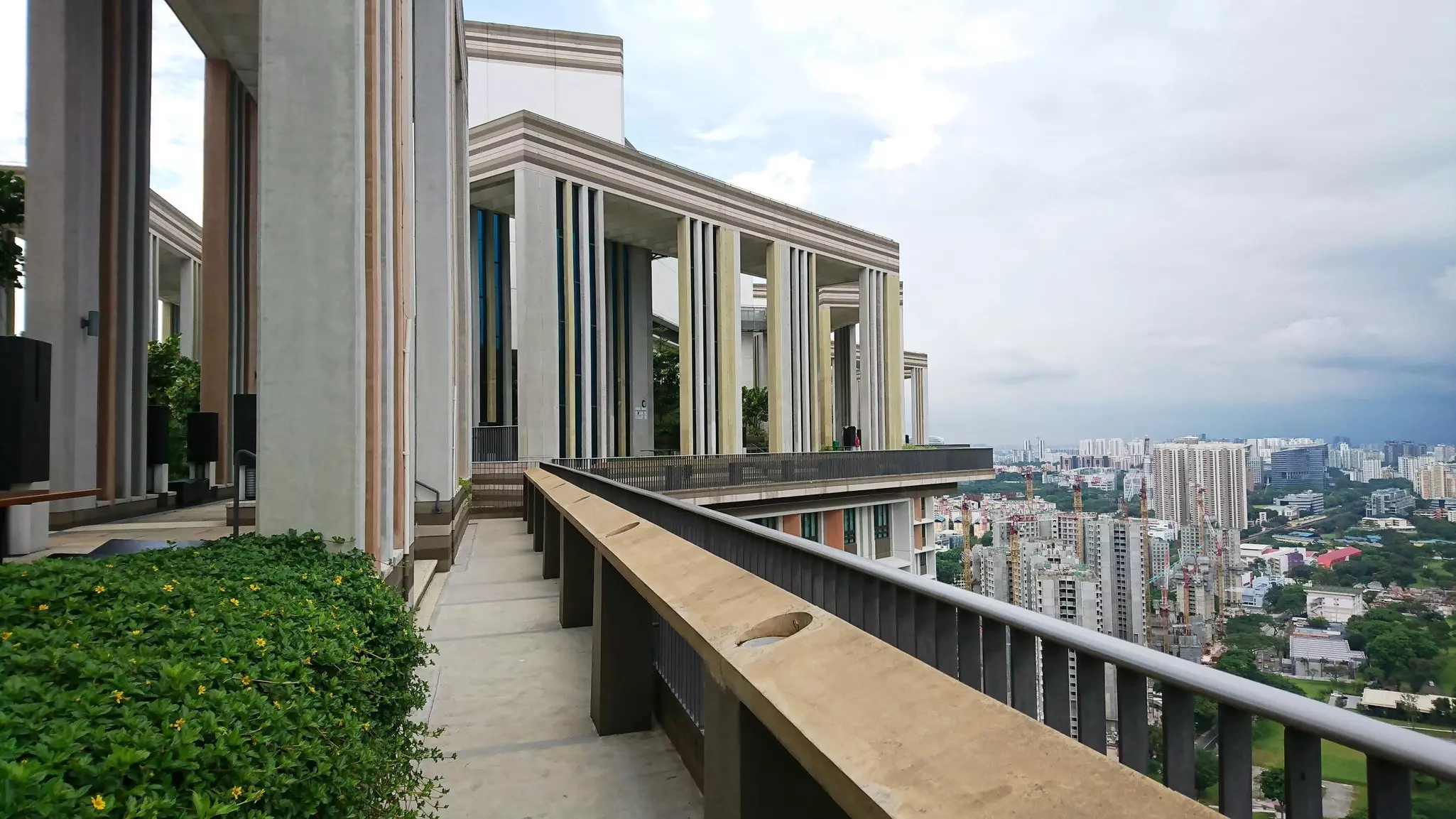 Benches and plantings are seen in a garden on the roof of a tall building. Other city towers are seen in the distance below.