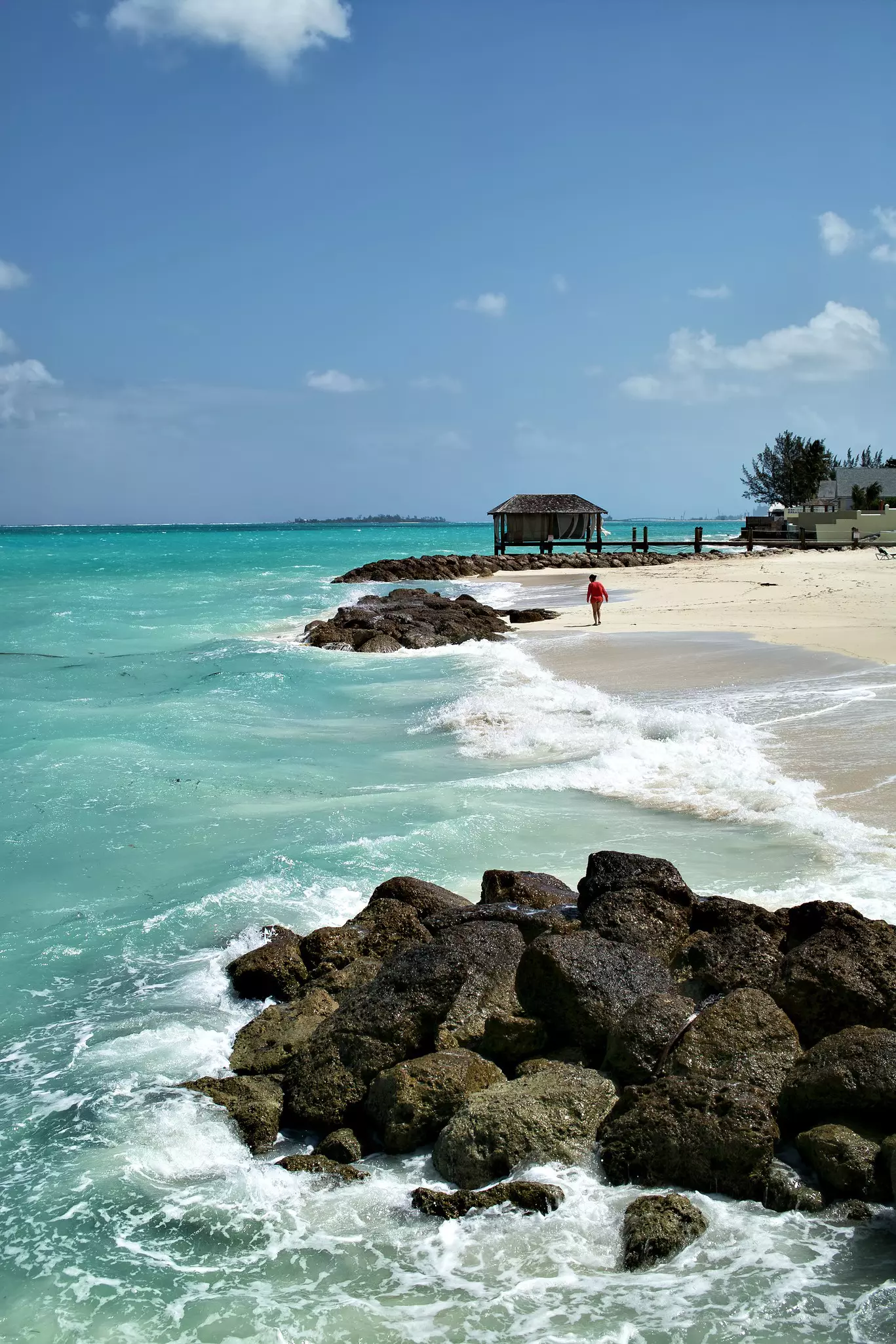Someone walks toward a thatched hut on the beach in Nassau, Bahamas.