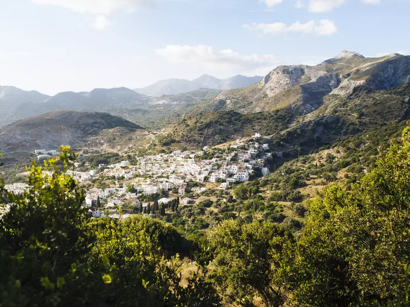 A whitewashed village sits within lush mountains in Greece. 