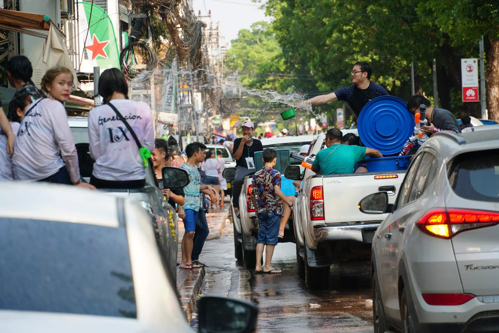 A man in the back of a pickup truck throws water onto a crowd in a city street during a celebration.