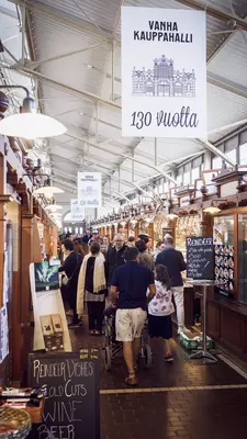 People walk past wooden stalls in a market hall in Helsinki.