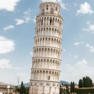 The Leaning Tower of Pisa with a red flag on top, tilting against a blue sky with white clouds, a crowd on the grass below.