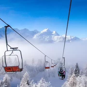 Ski lifts above snow-covered trees with a snow-covered mountain range in the background