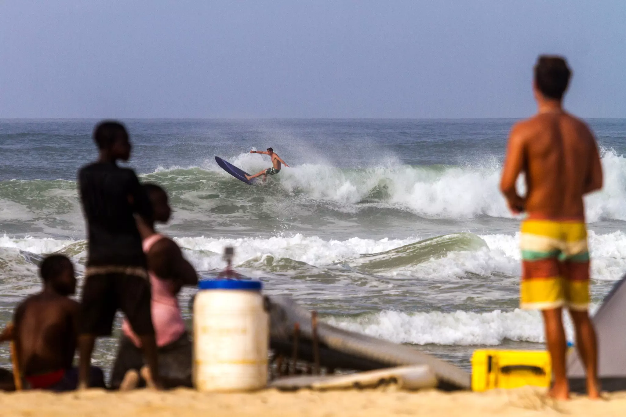 A man surfs rough waves as people in soft focus watch from the beach in the foreground.