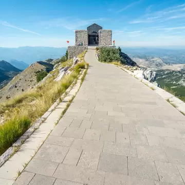 Long paved walkway along a grassy ridge to a granite tomb building, hazy mountain ranges stretching away on both sides