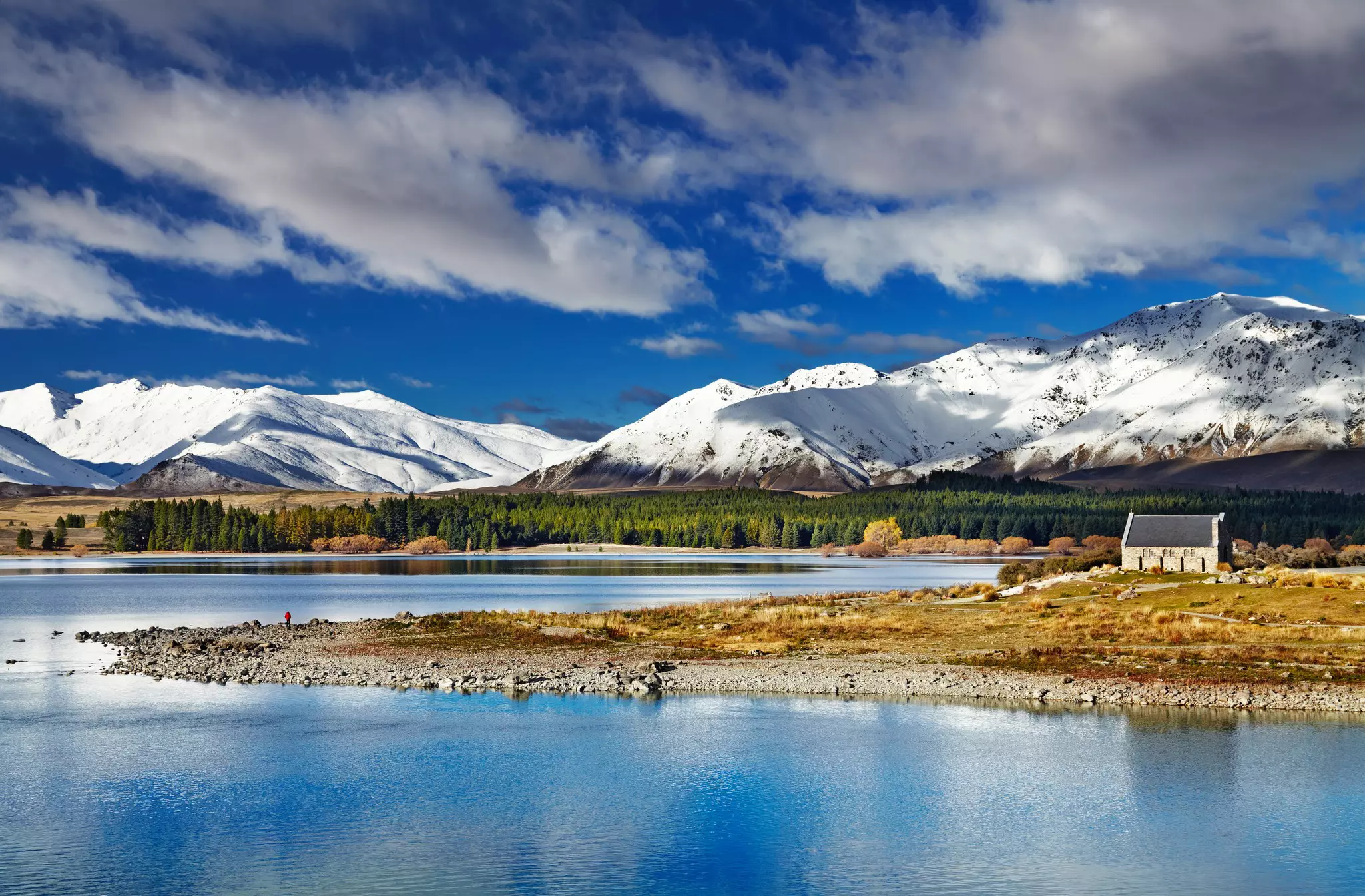a small hut with snow-covered mountains in the background and a lake in the foreground