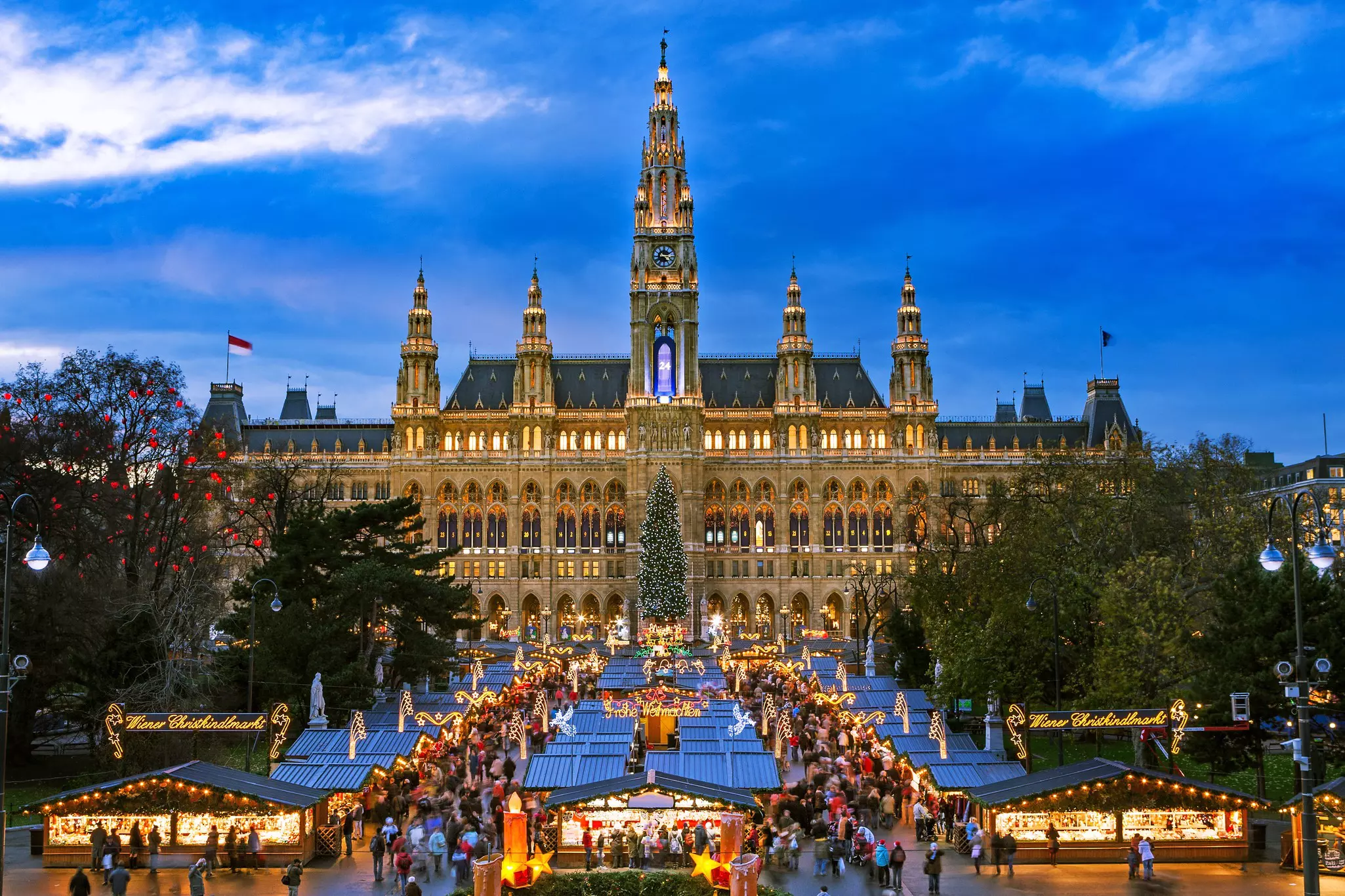 A huge town hall building stands above a square packed with market stalls lit with festive lights.