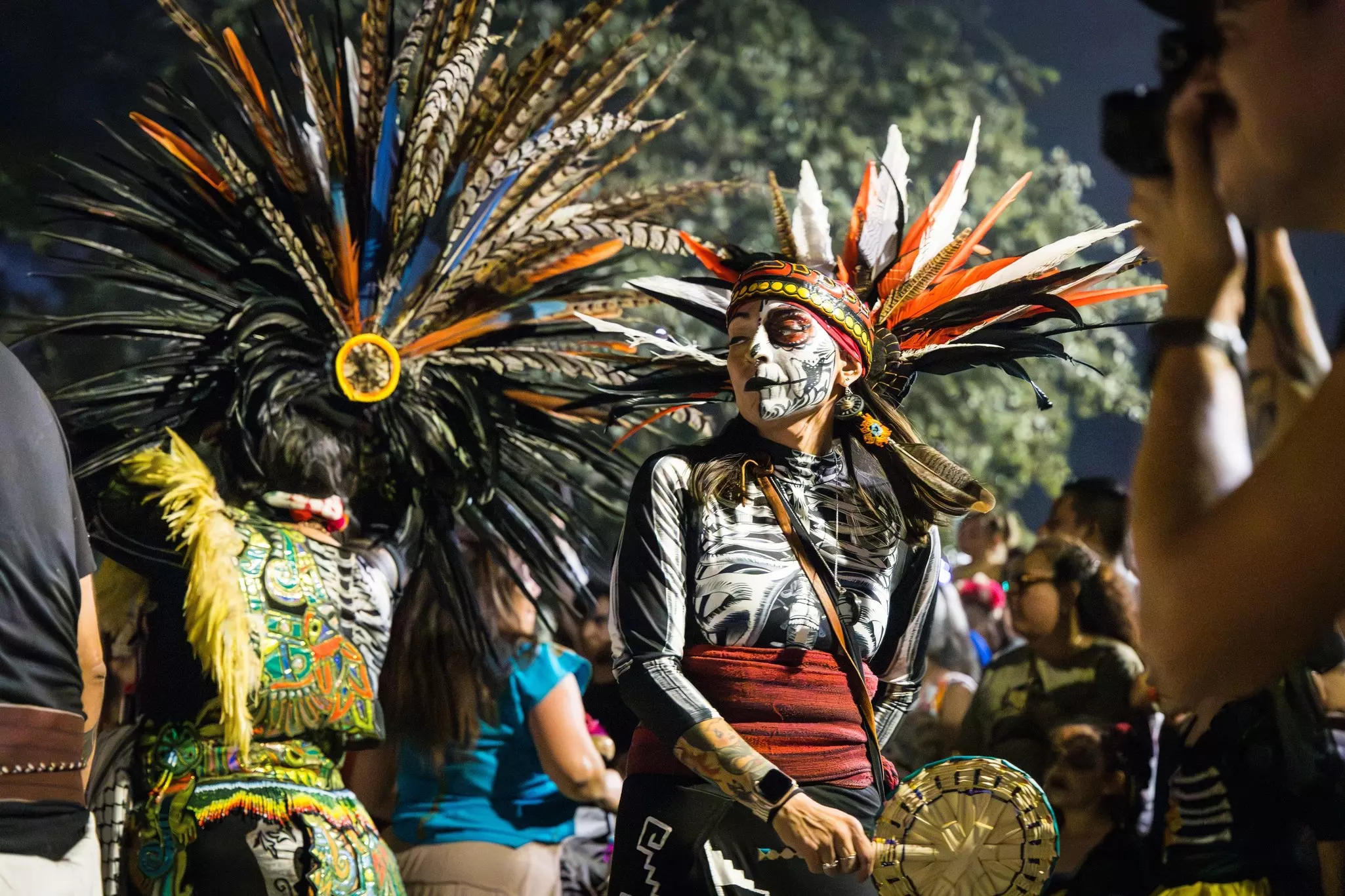 Indigenous people in headdresses, makeup and colorful outfits, performing a traditional Aztec dance