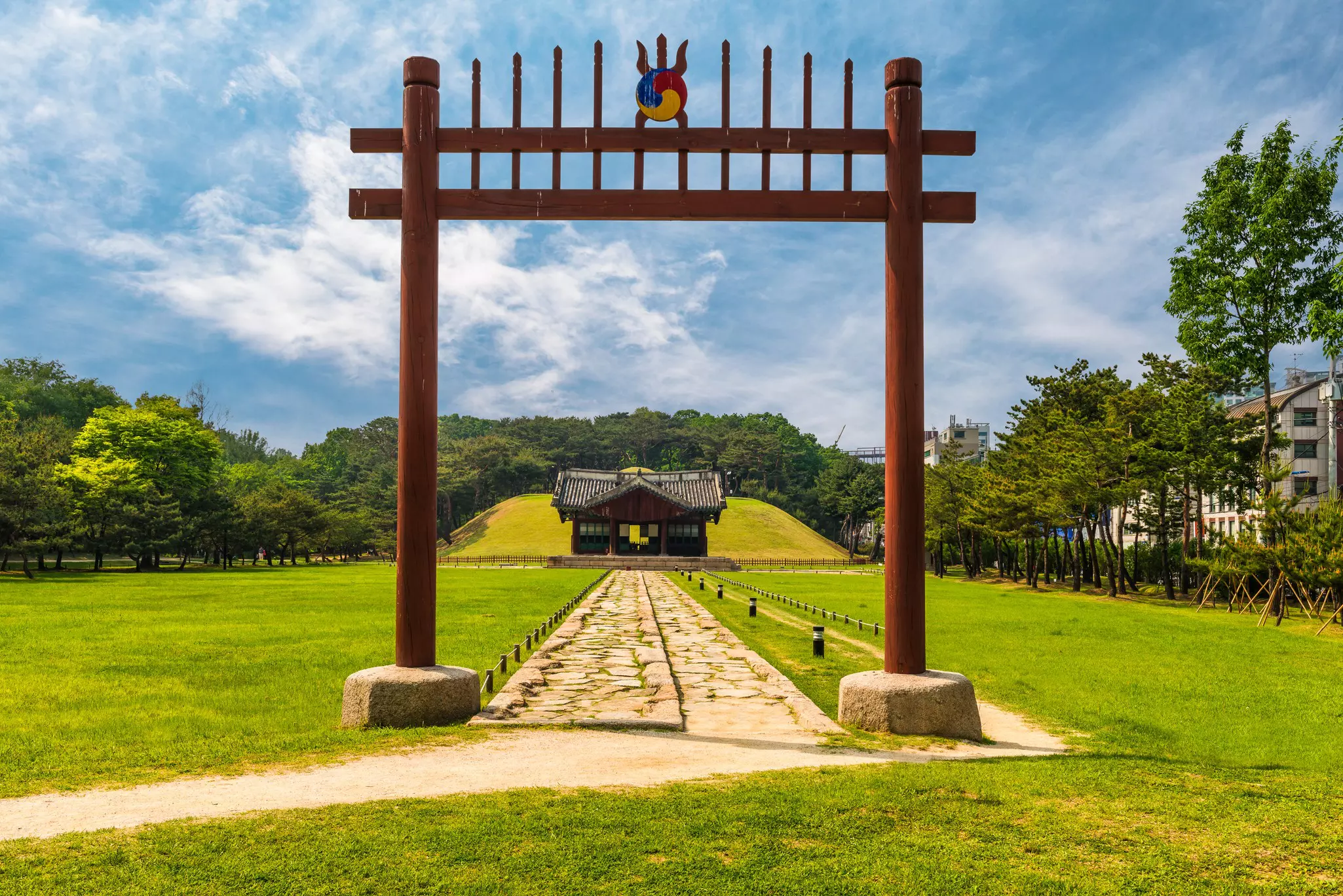 A gateway and pathway leading to a tomb in parkland.