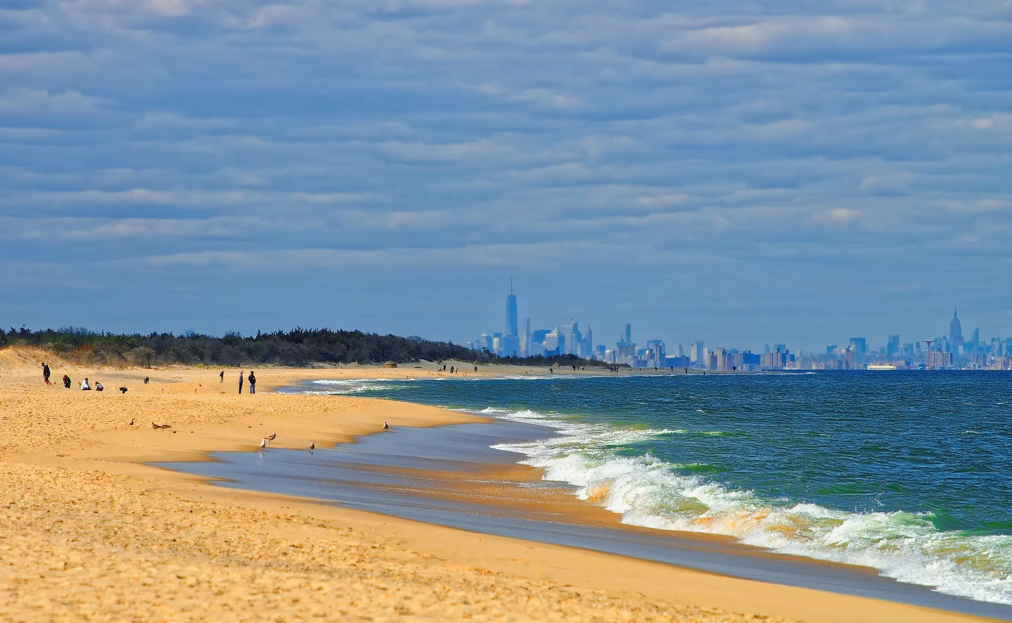 Sandy shoreline with ocean to the left and New York City skyline in the distance.