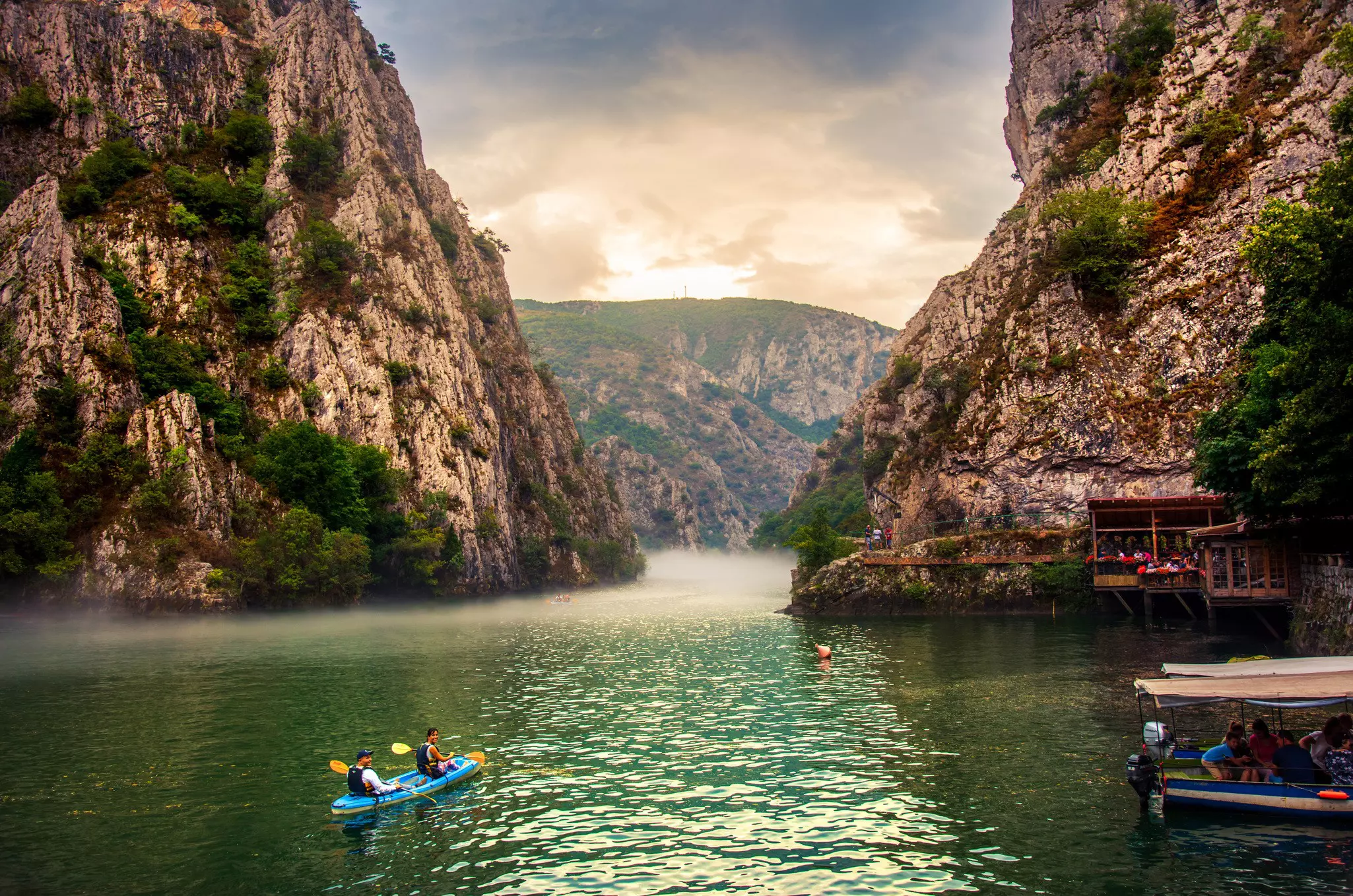 Kayakers paddle between the sheer rock sides of a canyon with mist on the water.