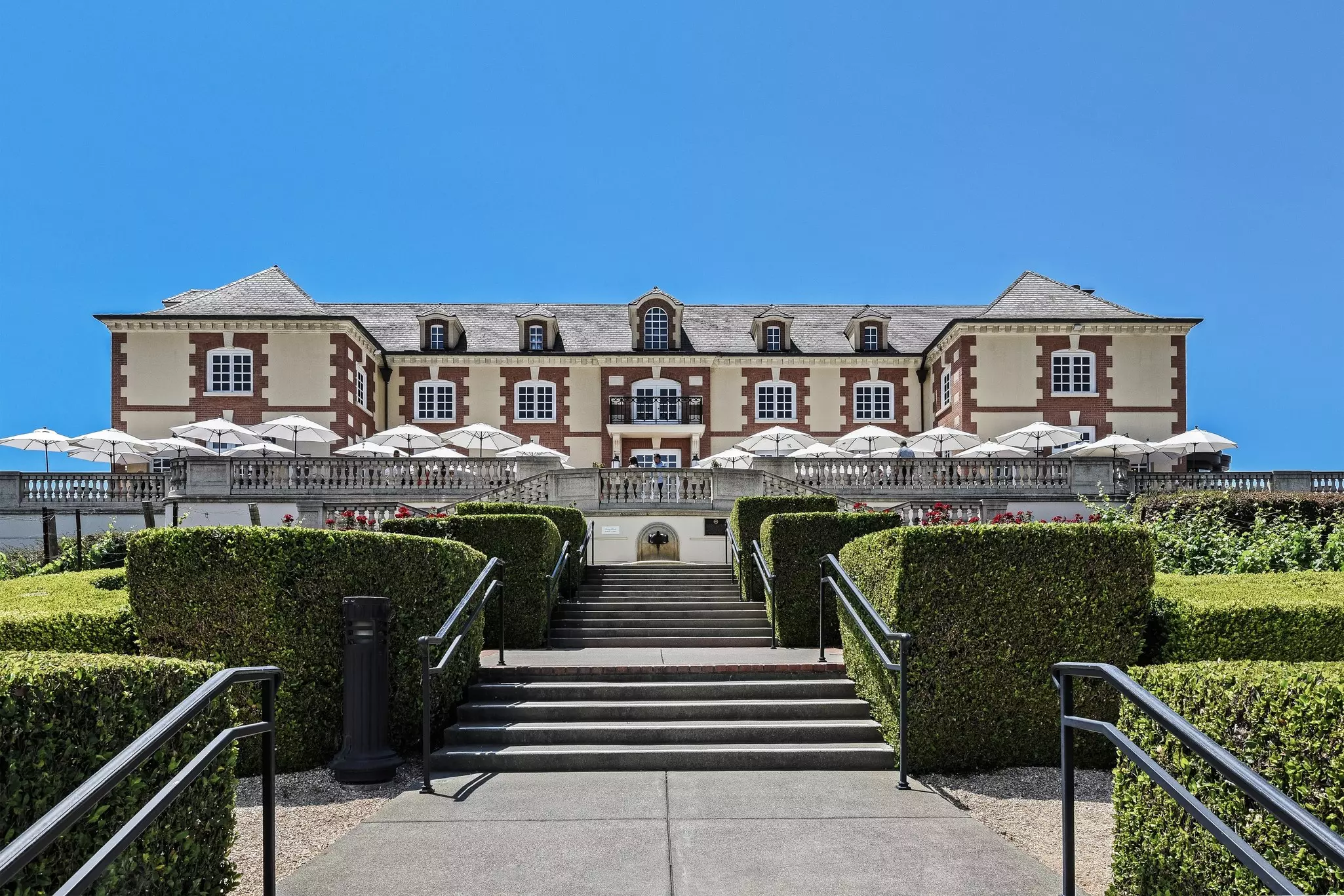 A large multicolor brick building with stairs leading up to it. White umbrellas are arranged on a patio outside the entrance