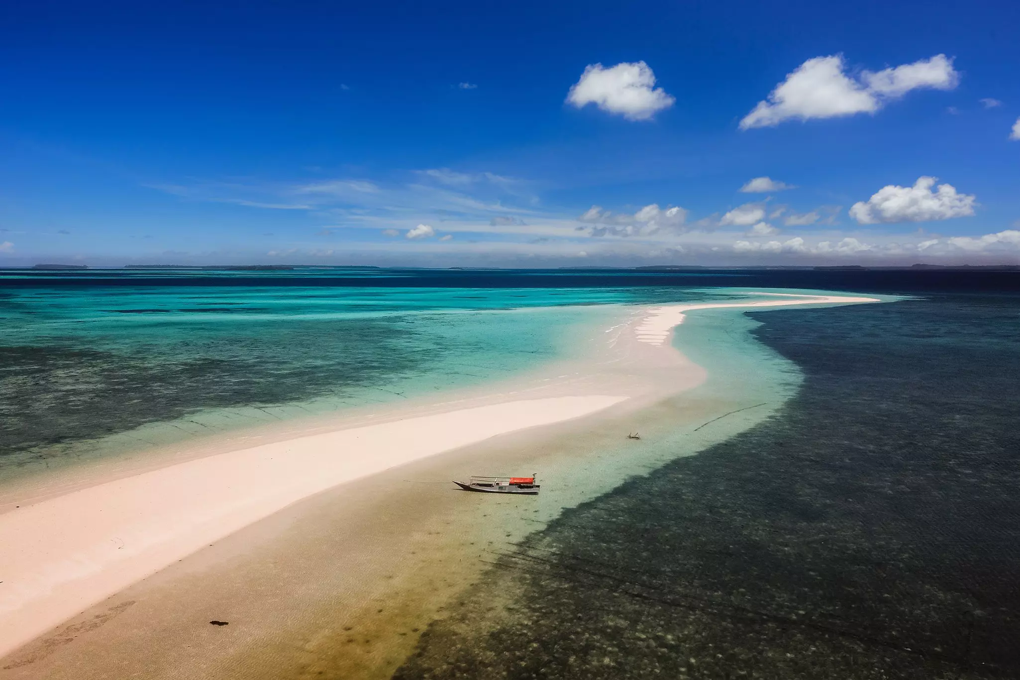 A sandbar in a turquoise sea with a small fishing boat