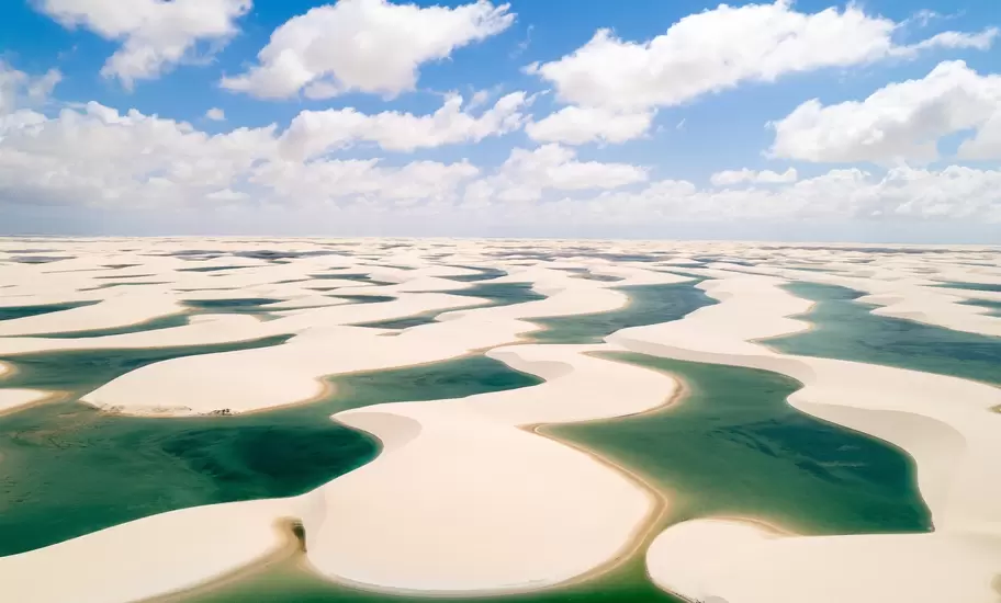Lençóis Maranhenses dunes in Brazil, white sand ridges between green rain-filled lagoons under puffy clouds
