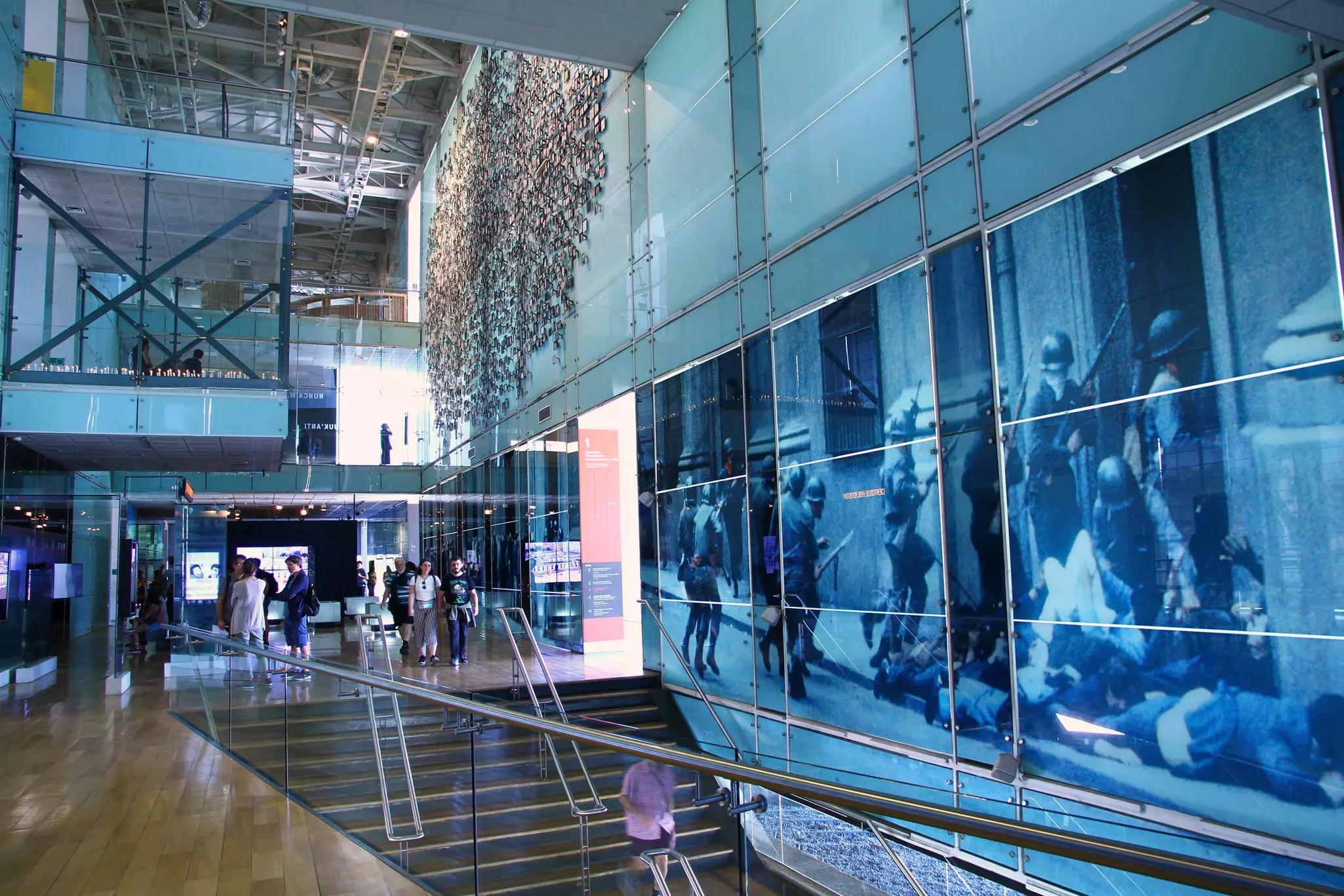 The interior of a museum, with large photographs lining one wall and glass-fronted galleries visible across the atrium.