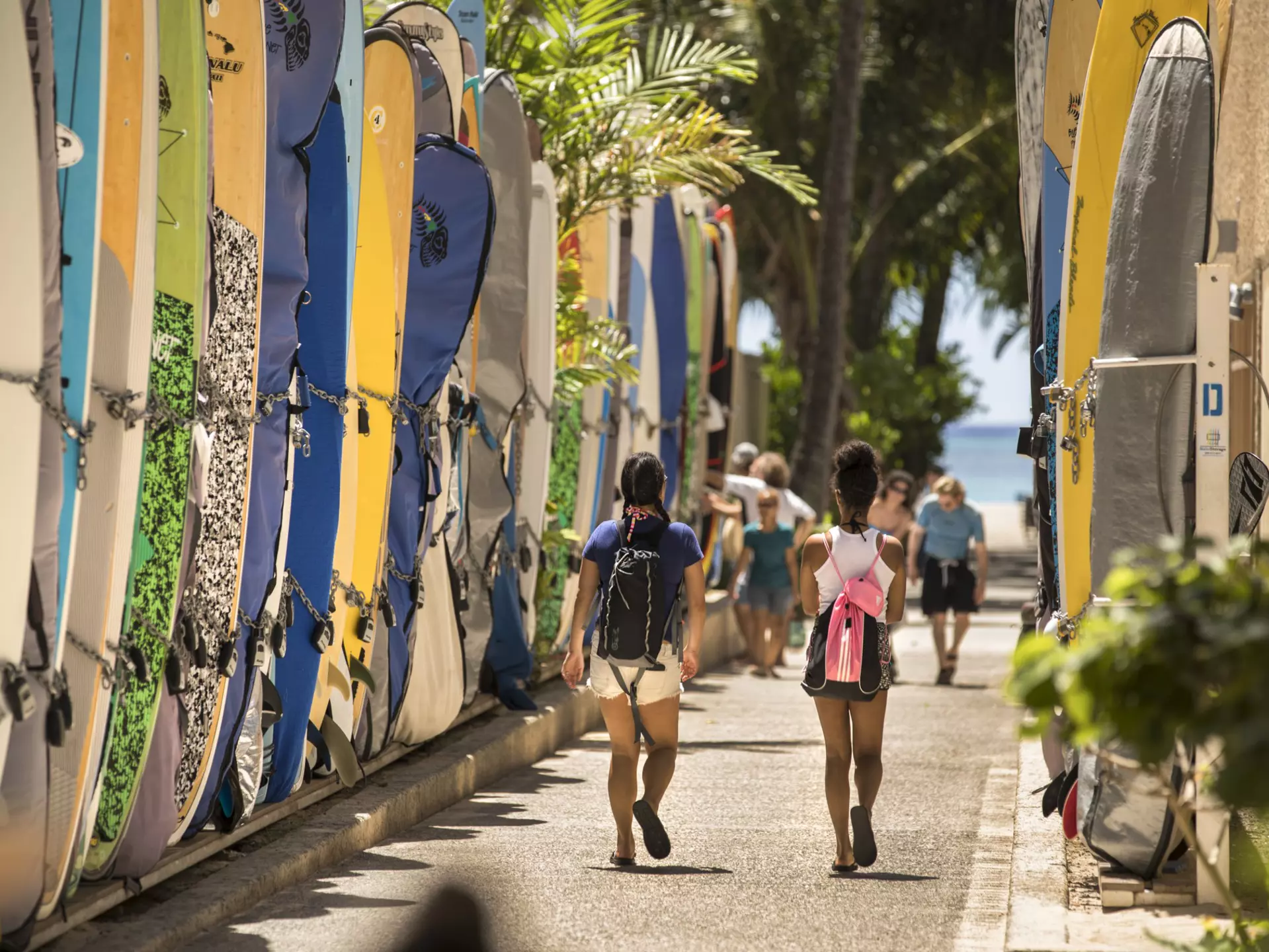Honolulu: Tourists walk by a surfboard lined alley off the commercial shopping district of Kalakaua Avenue by Waikiki Beach.  Surfboards are locked up here when not in use.
855557540