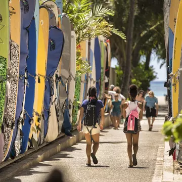 Honolulu: Tourists walk by a surfboard lined alley off the commercial shopping district of Kalakaua Avenue by Waikiki Beach.  Surfboards are locked up here when not in use.
855557540