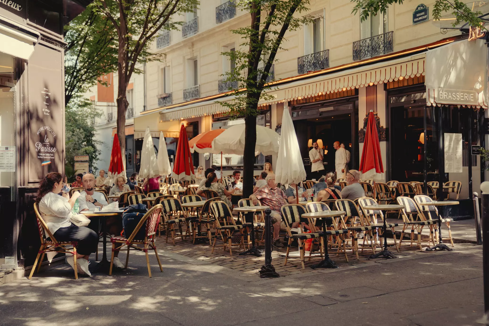 People sit on chairs on a terrace in the sun outside a bistro