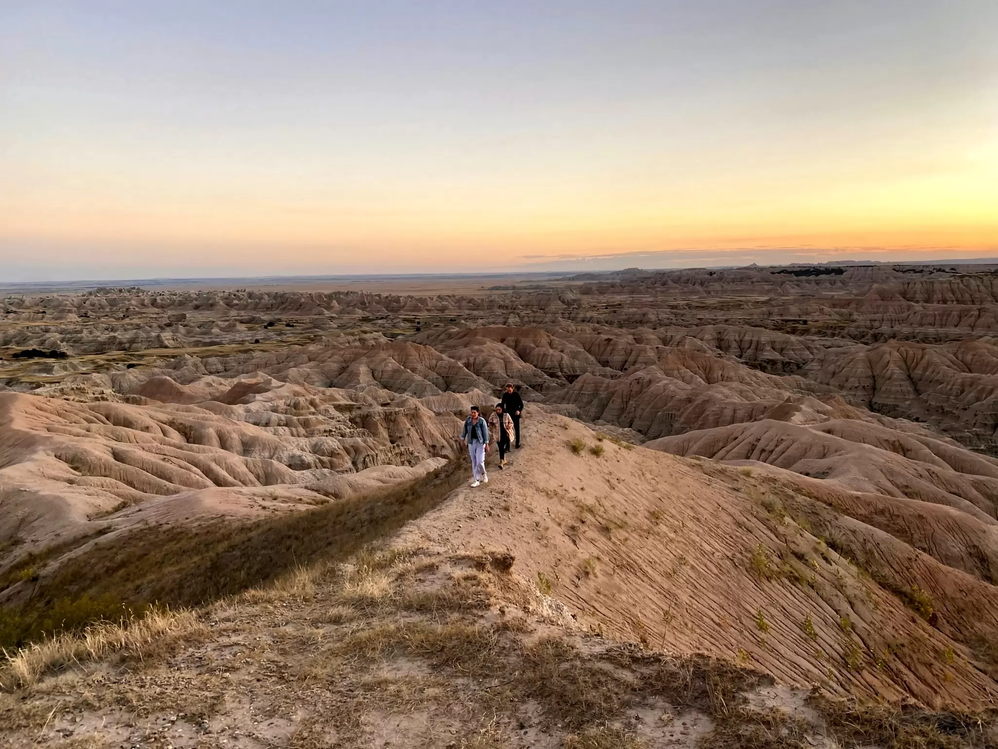 People walk on a trail over rock formations at sunset.