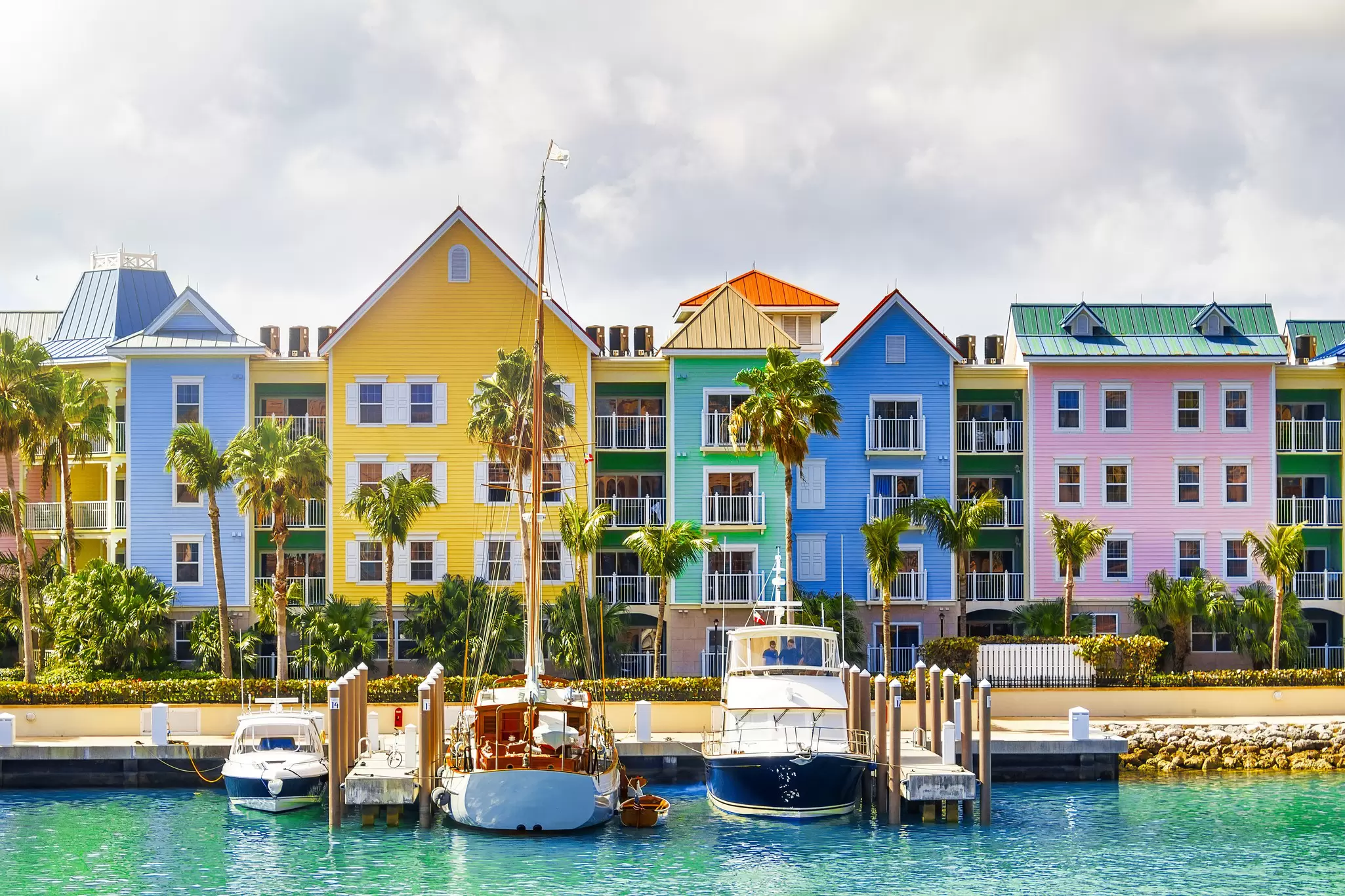 A row of pastel-painted houses on the shore with boats docked nearby at a small harbor.