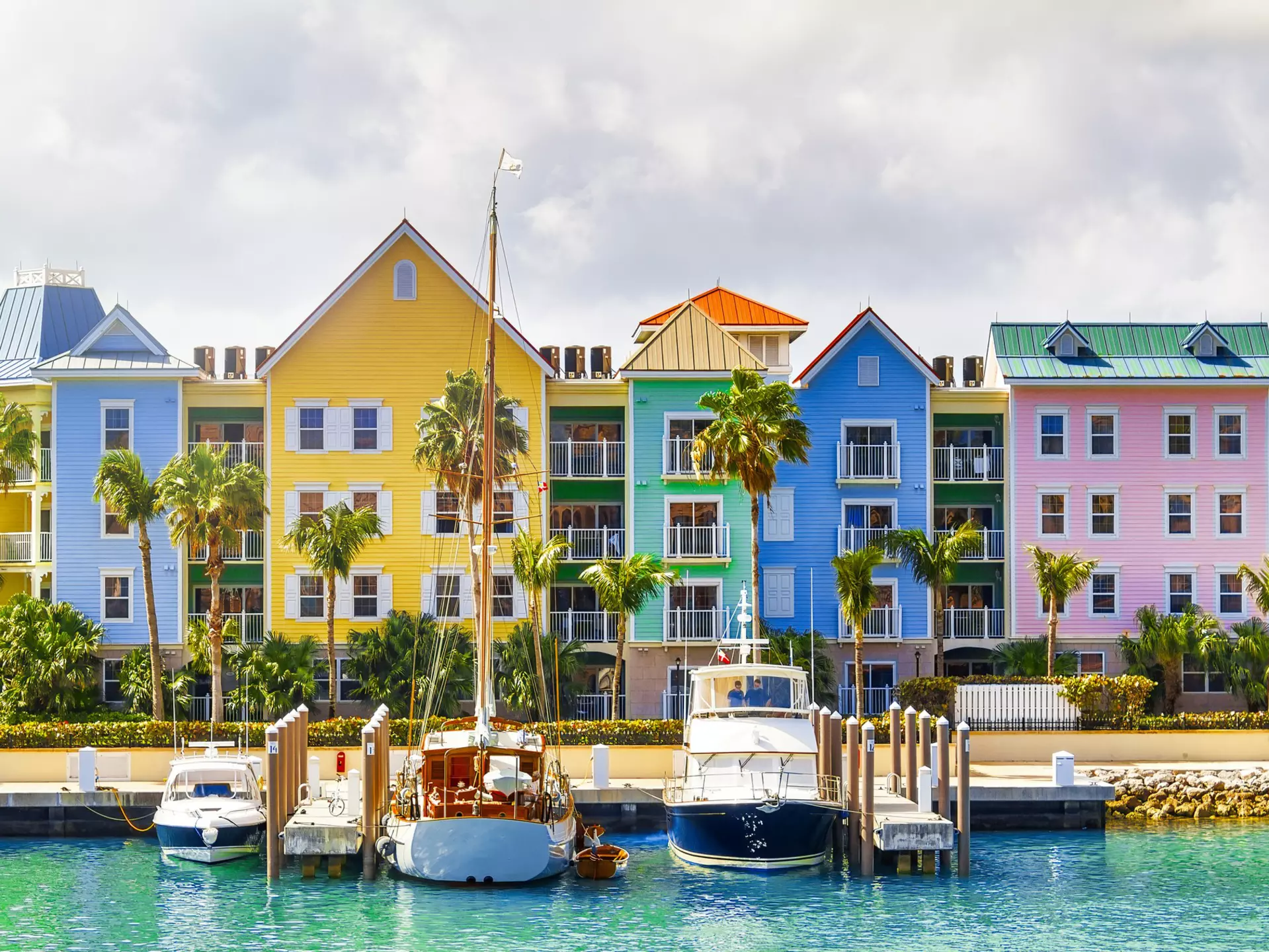 A row of pastel-painted houses on the shore with boats docked nearby at a small harbor.