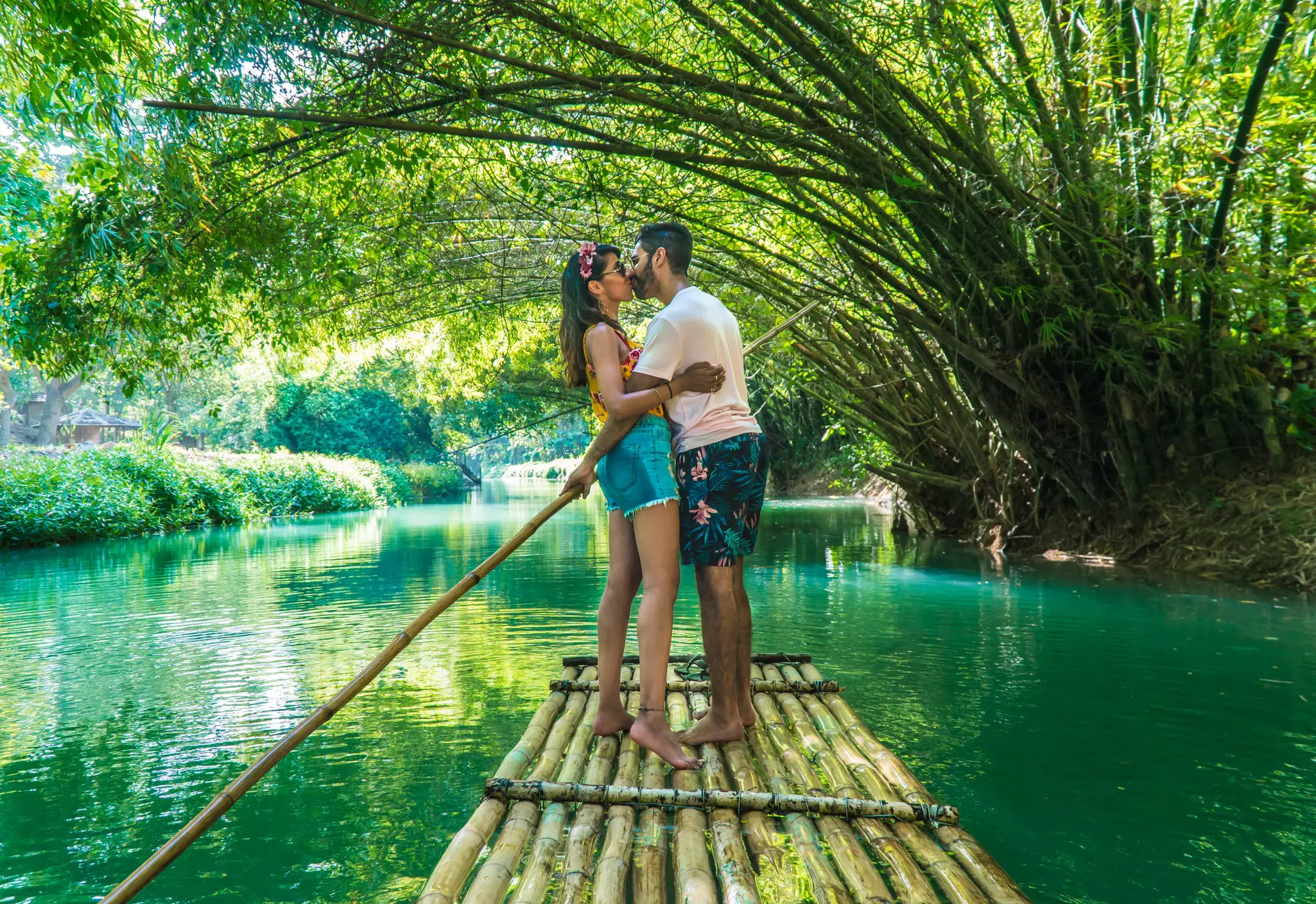 Happy couple kissing and taking a romantic ride down Martha Brae river, on bamboo raft.