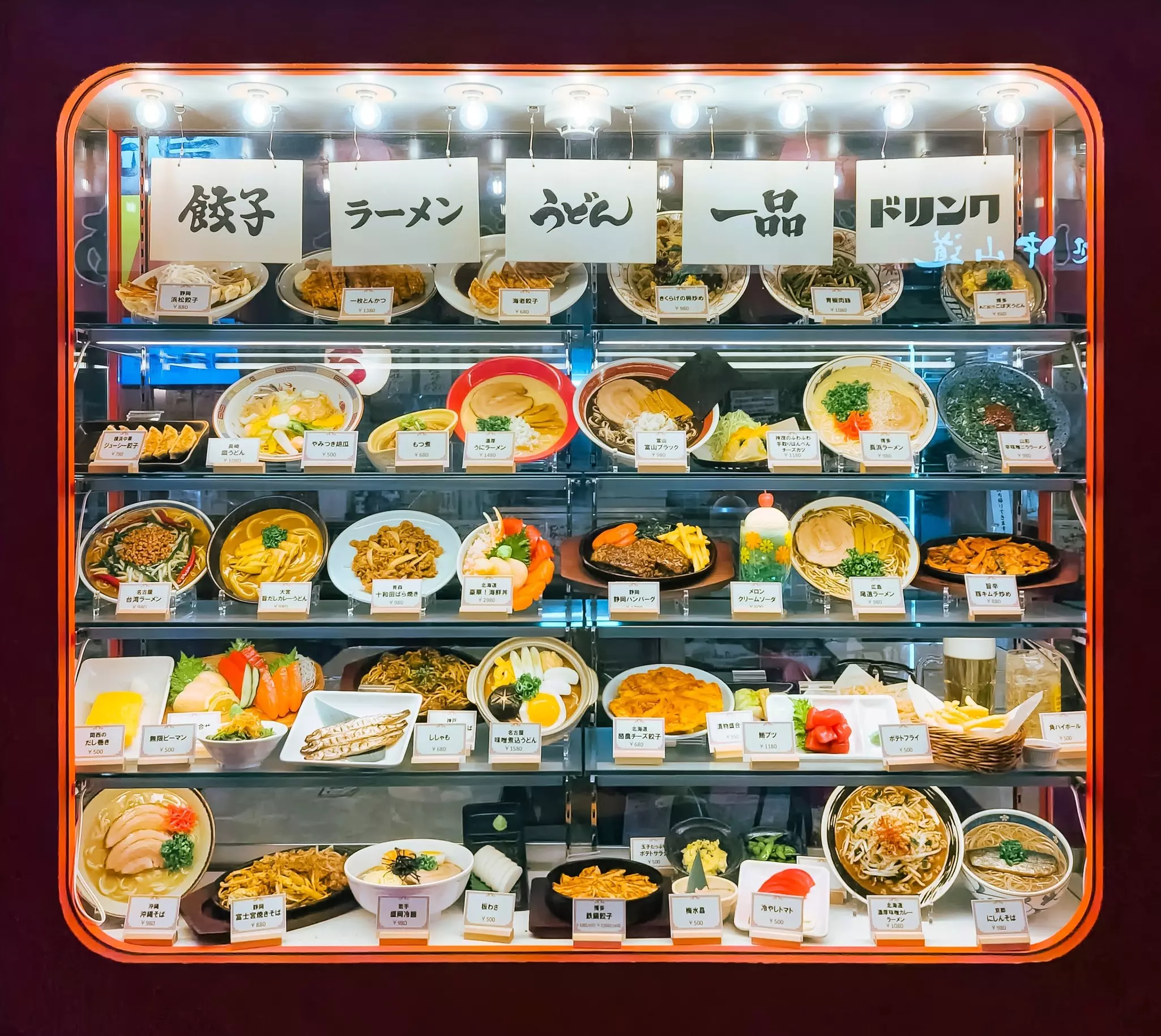 Five shelves with plates of food displayed in a shop window in Tokyo