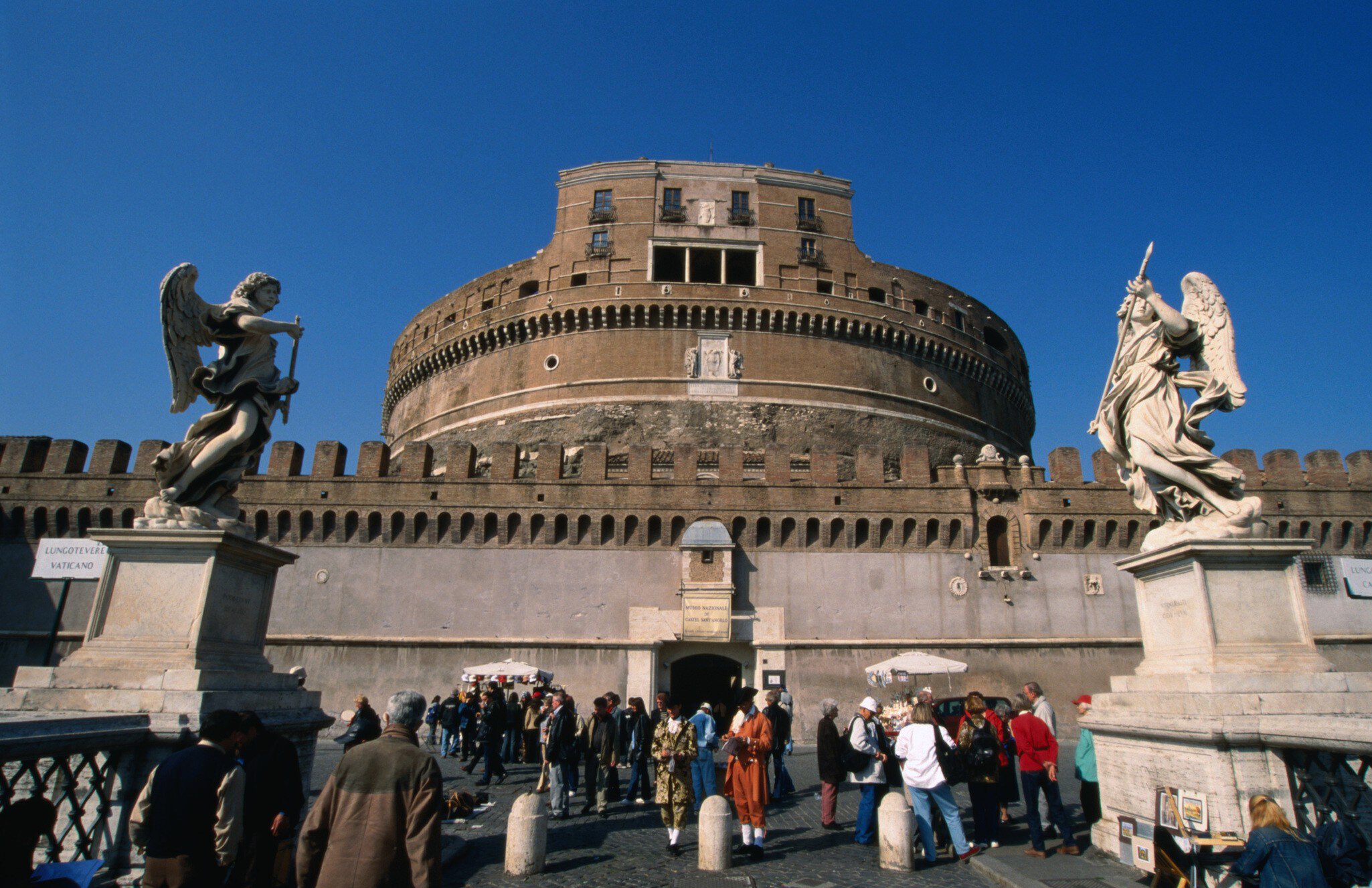 Tourists on the Pont Sant'Angelo make their way past the angels by Bernini and his pupils through to the heavily fortified Castel Sant'Angelo, Rome.