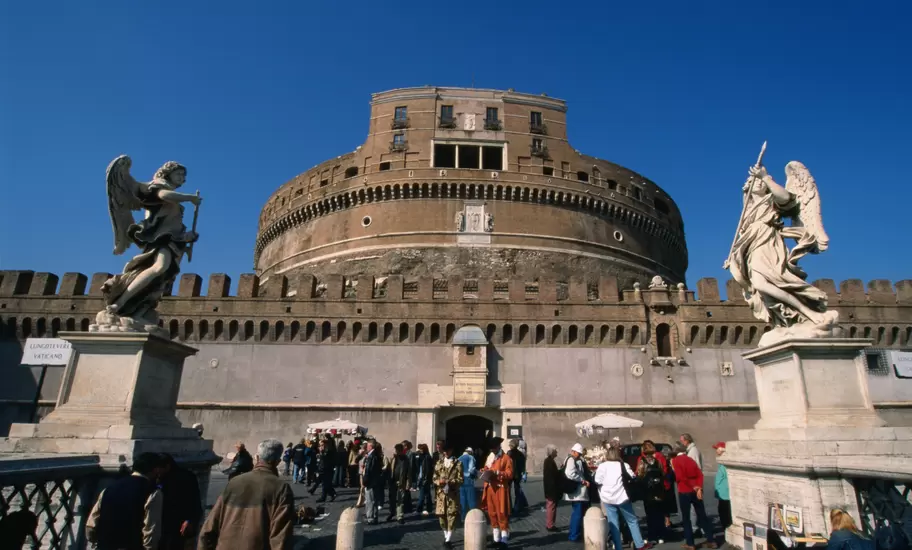 Tourists on the Pont Sant'Angelo make their way past the angels by Bernini and his pupils through to the heavily fortified Castel Sant'Angelo, Rome.