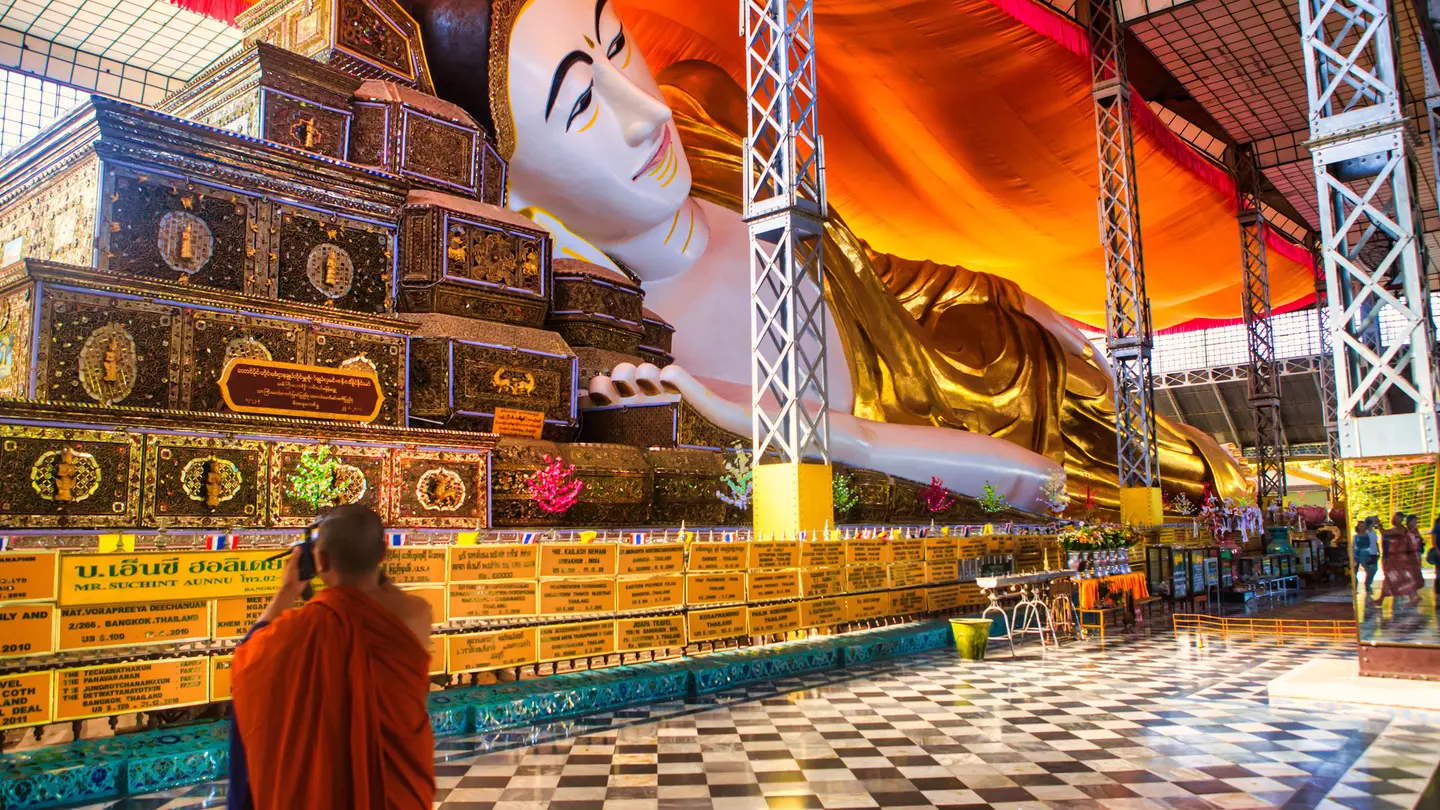 A monk wearing orange robes takes a photograph of a huge reclining Buddha