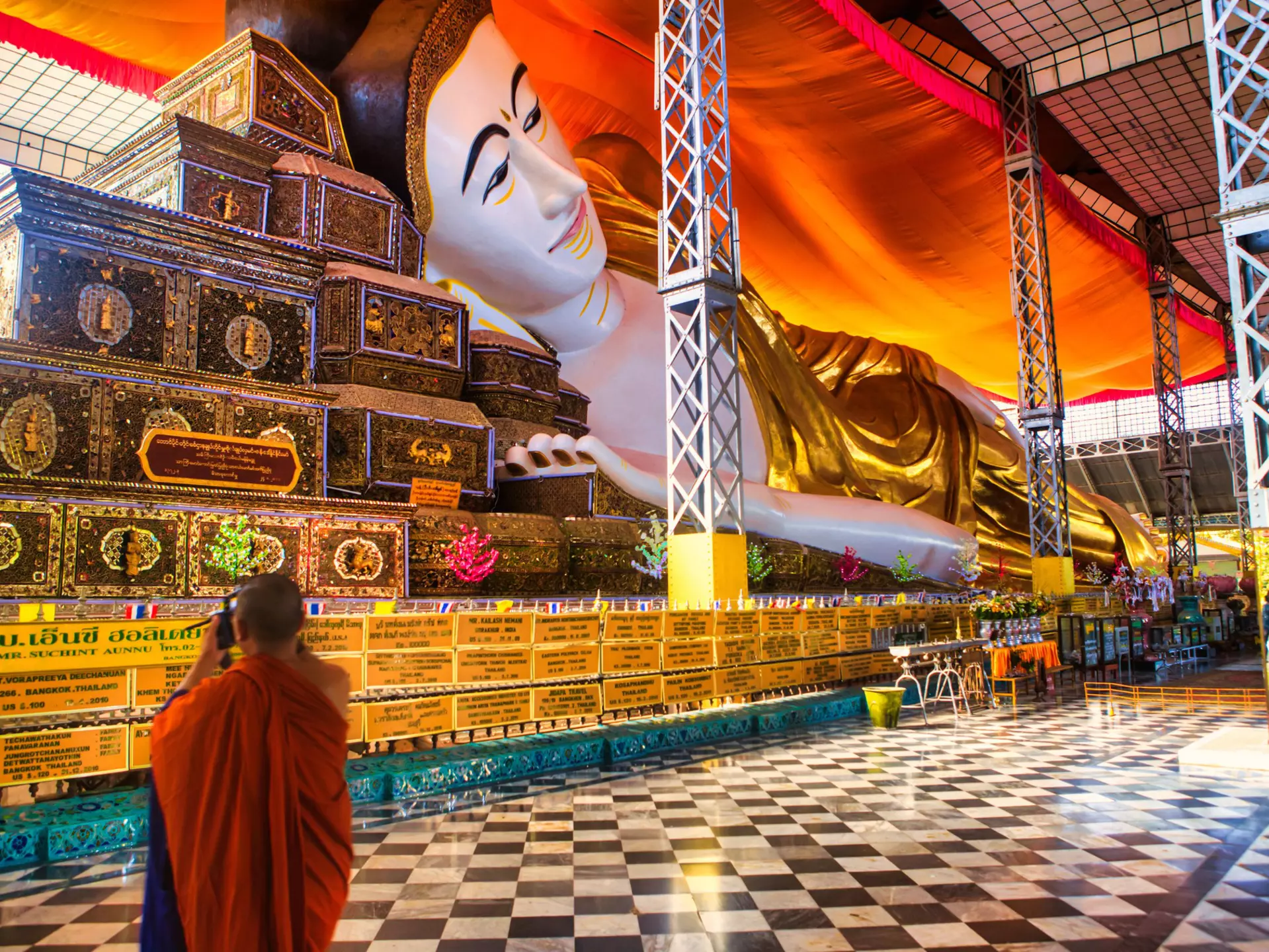 A monk wearing orange robes takes a photograph of a huge reclining Buddha