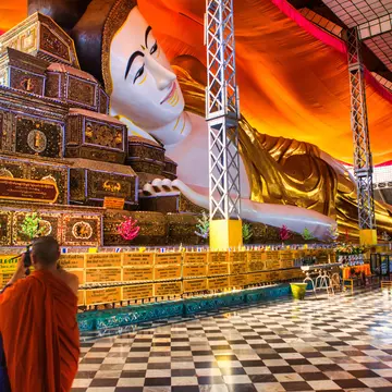 A monk wearing orange robes takes a photograph of a huge reclining Buddha