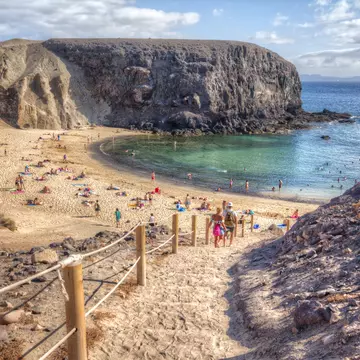 People descend steps to small beach with blue waters, in between jagged rock formations