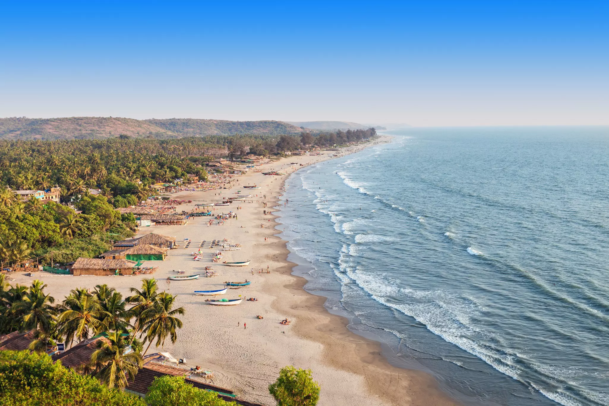A vast sandy beach with waves crashing on the shore. Several cabins and small thatched structures line the beach.