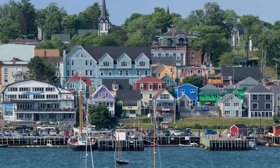 Colourful wooden buildings and a church spire above Lunenburg harbour, Nova Scotia, with sailboats on the water
