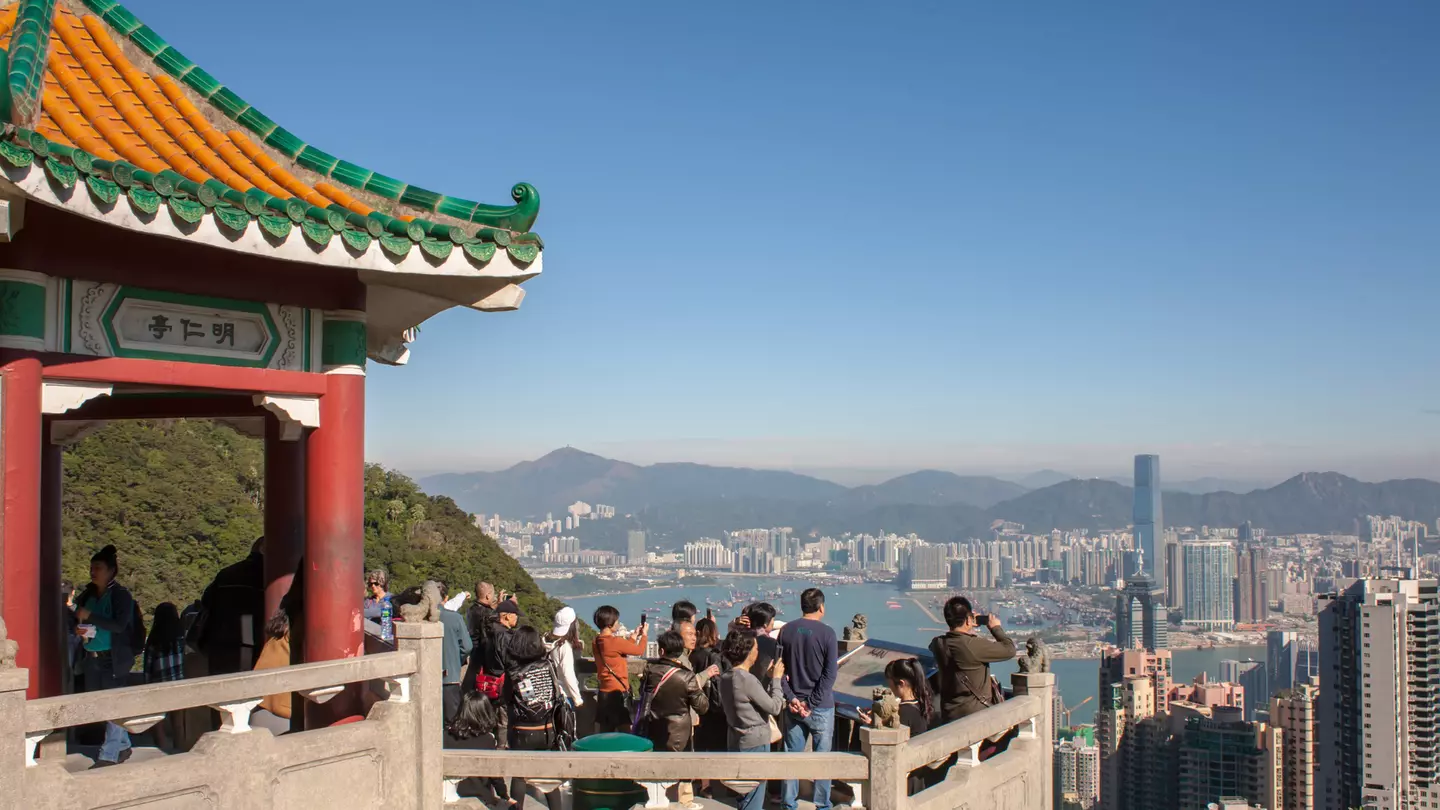 Tourists crowd at a Victoria Peak viewpoint looking out over the rooftops of Hong Kong.